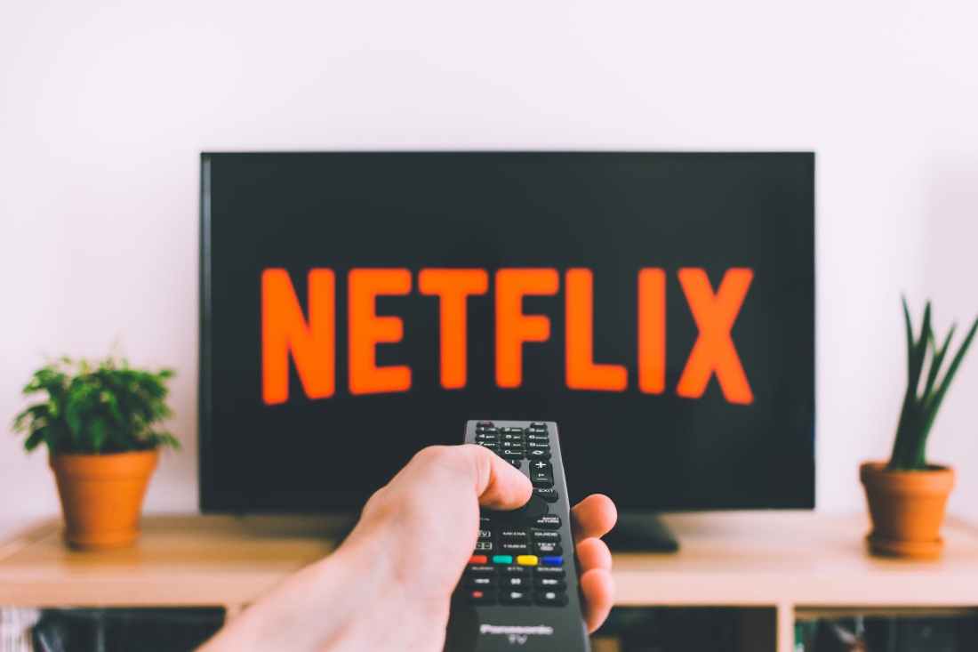 closeup photo of person holding panasonic remote control in front of turned on smart television